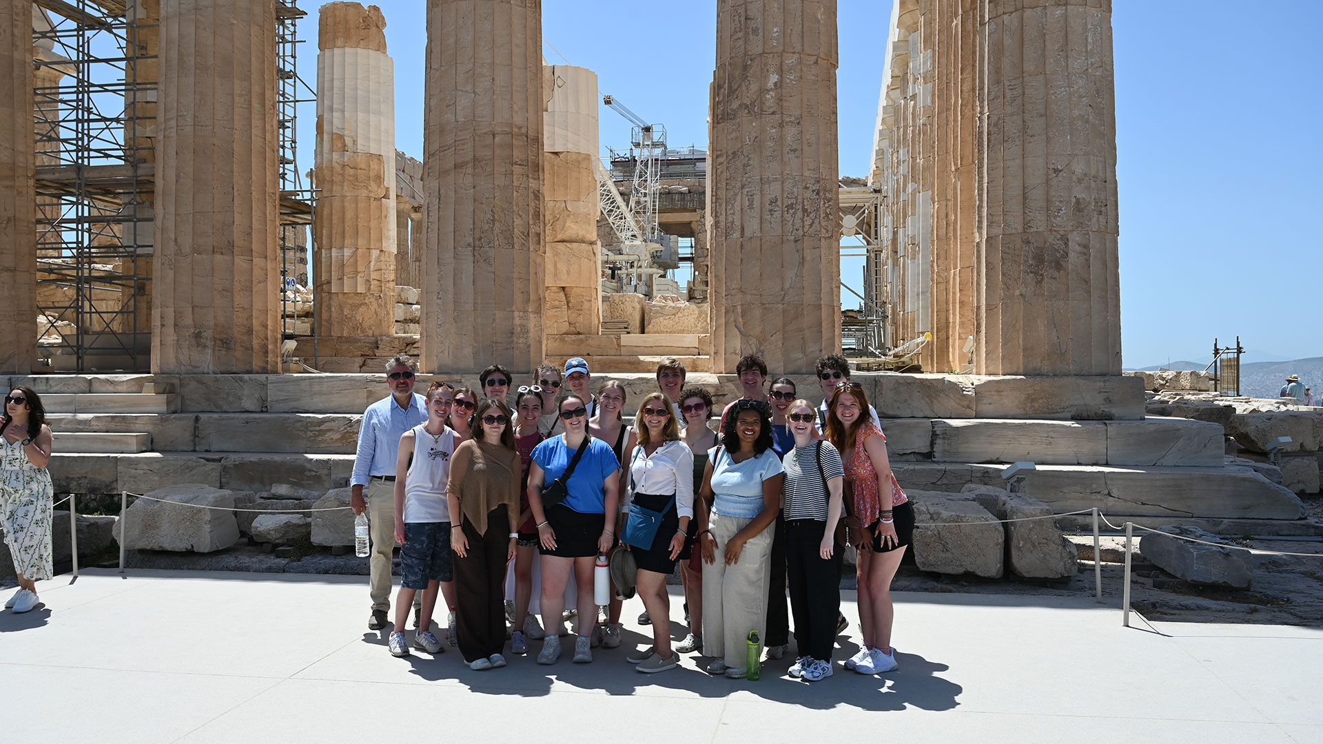 A group of economics students and faculty stand for a photo in front of Grecian ruins.