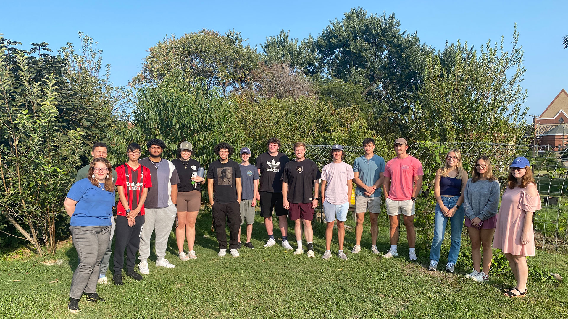 A group of economics students stand in a semi circle in a green space.