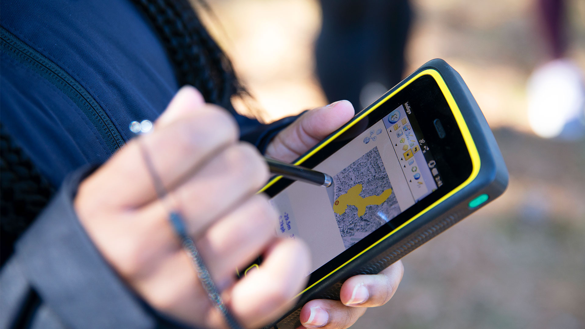A Christopher Newport ecology student uses a stylus on a rugged tablet to map data points and habitat areas over an aerial field map.