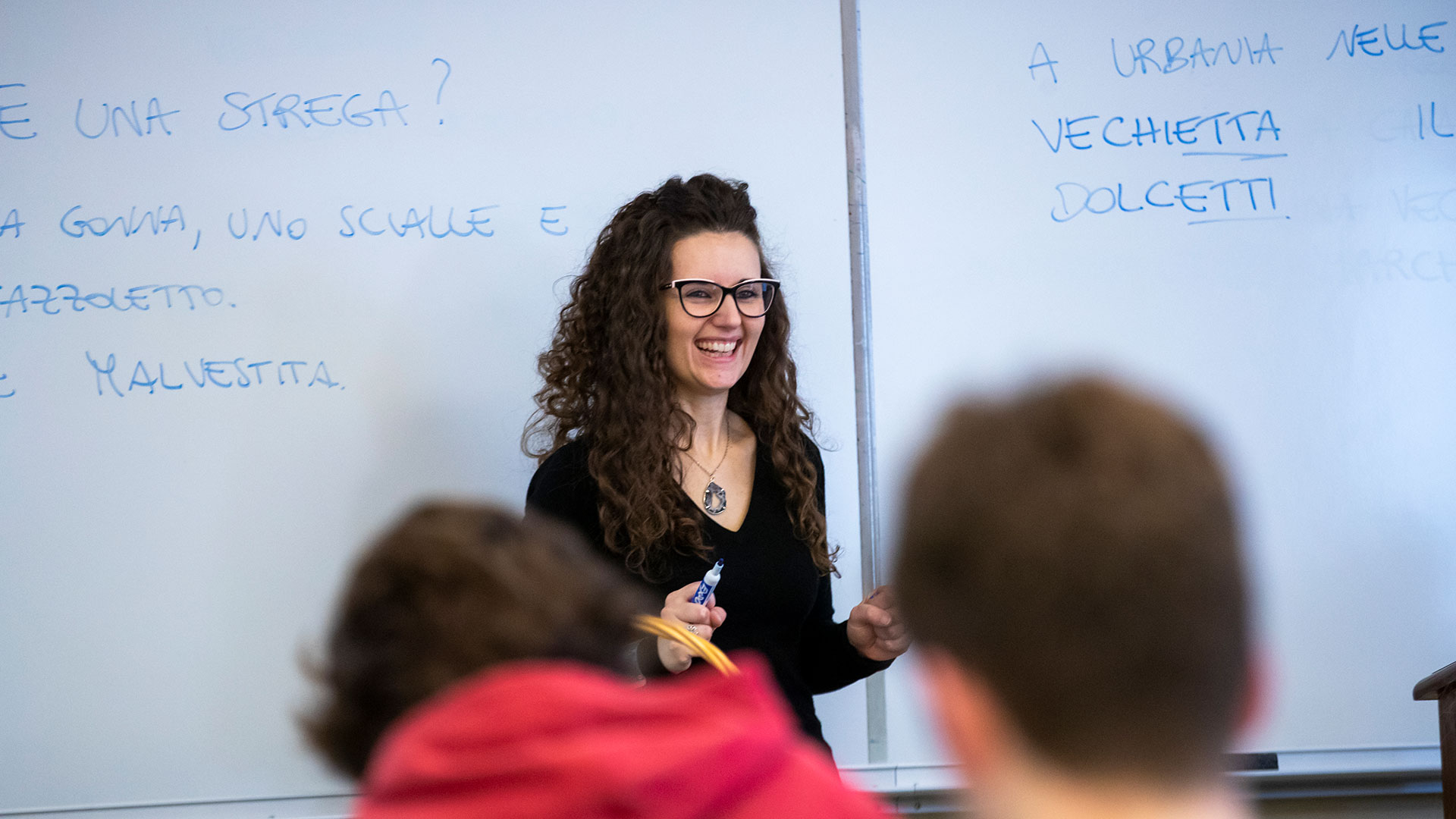 Smiling professor standing in front of a board with Italian grammar written on it