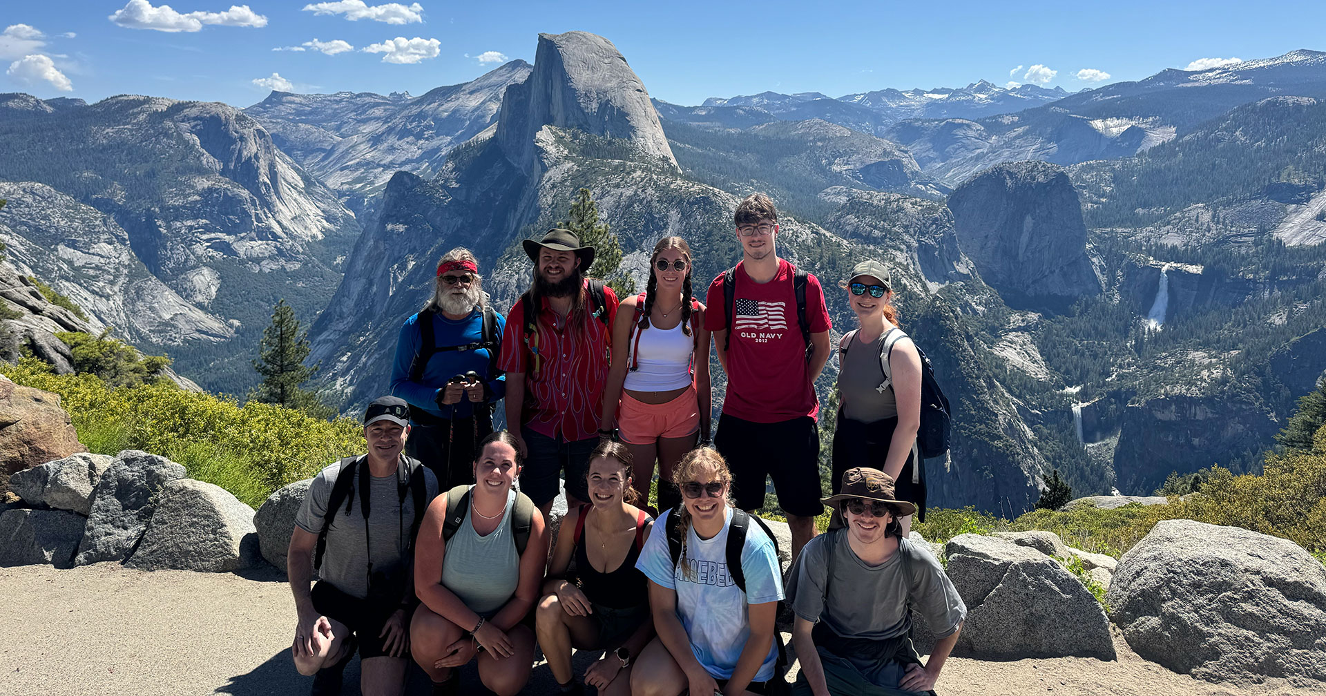 A group of students and faculty smile with a vast mountain range behind them.