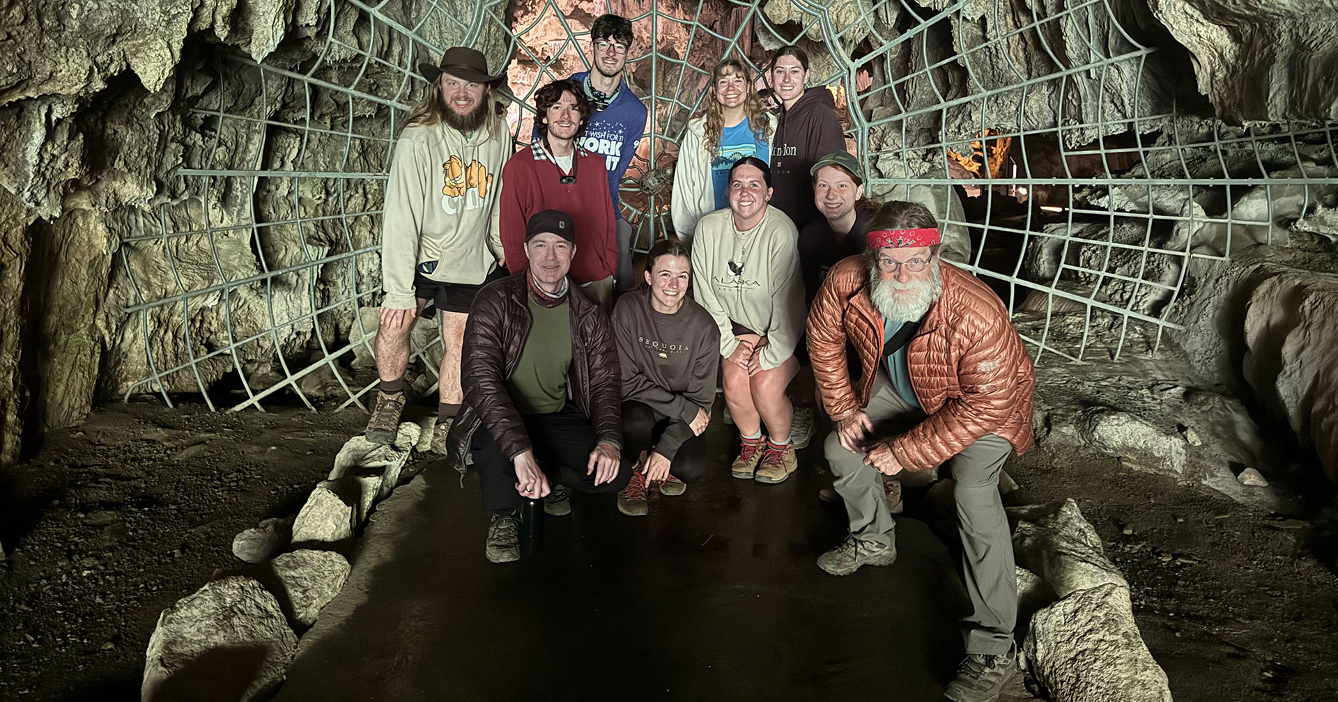 A group of faculty and staff standing a cave with webbing behind them