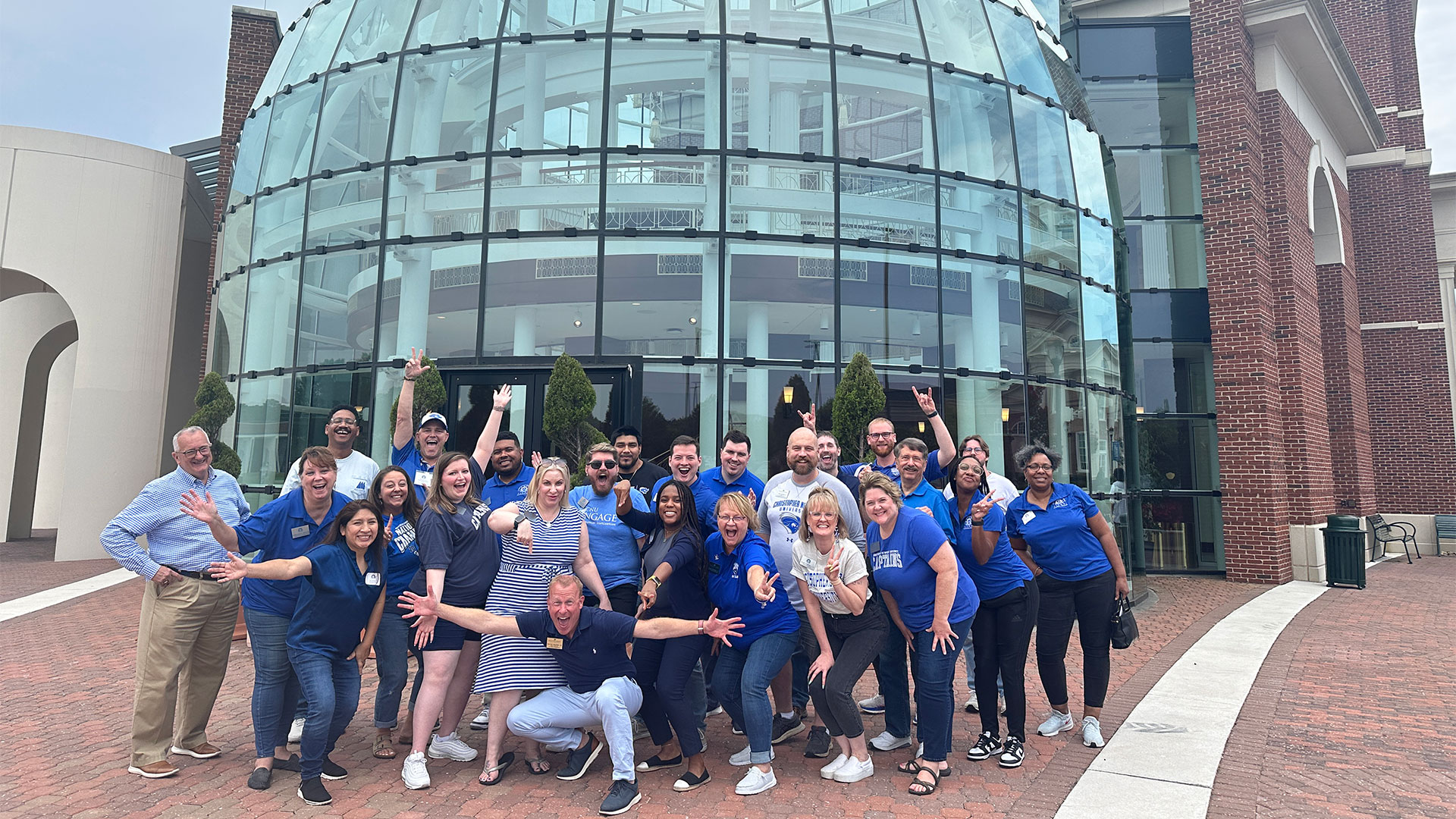 A group of alumni smile for a photo in front of the glass domes of the Mary M. Torggler Fine Arts Center