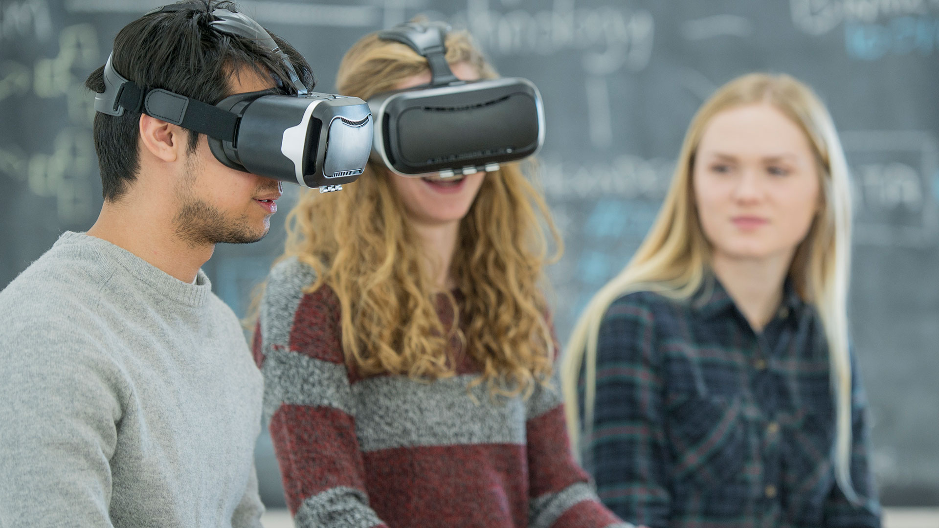 Two young adults wear virtual reality headsets in a classroom setting